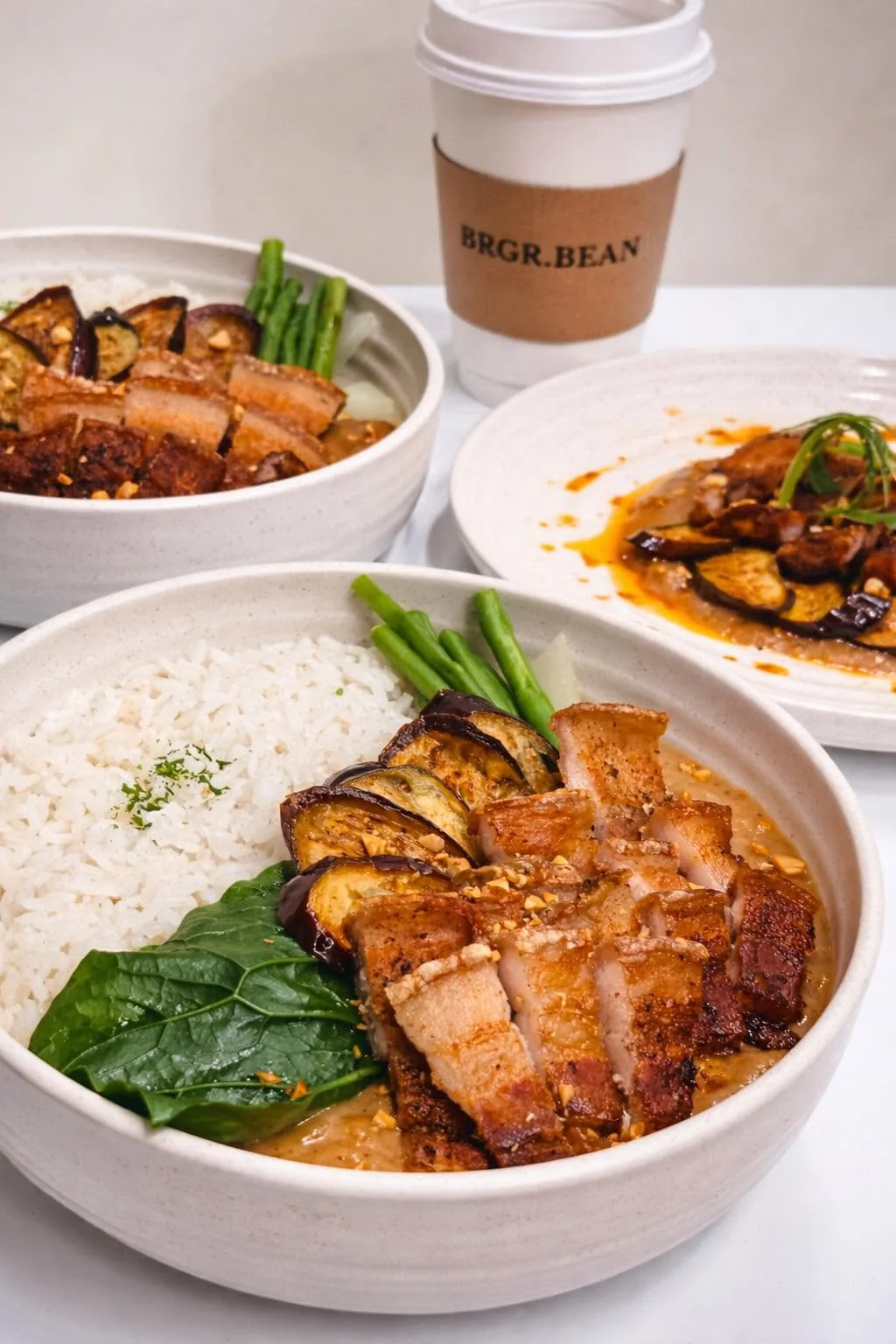 Crispy pork with rice and vegetables beside a BRGR.BEAN coffee cup